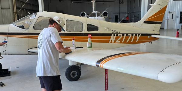 Man cleaning a small airplane wing in a hangar.
