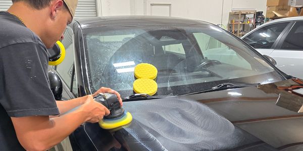 Man polishing black car hood in garage.