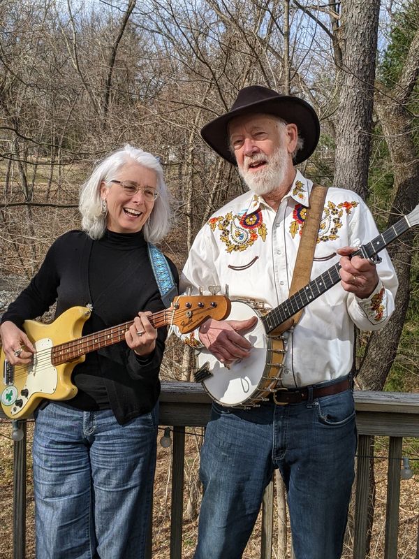 Two older adults playing string instruments outdoors on a wooden deck.
