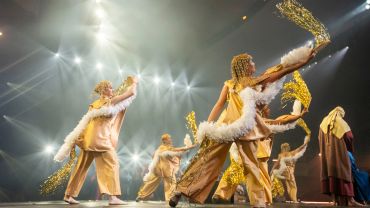 Performers in gold costumes dancing on stage.
