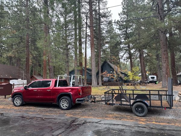 Red pickup truck towing a metal trailer in a forested residential area.