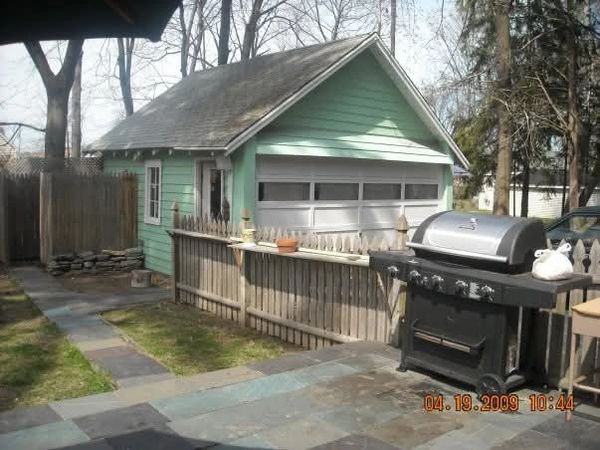 Small green garage behind a wooden fence with a grill in the foreground.