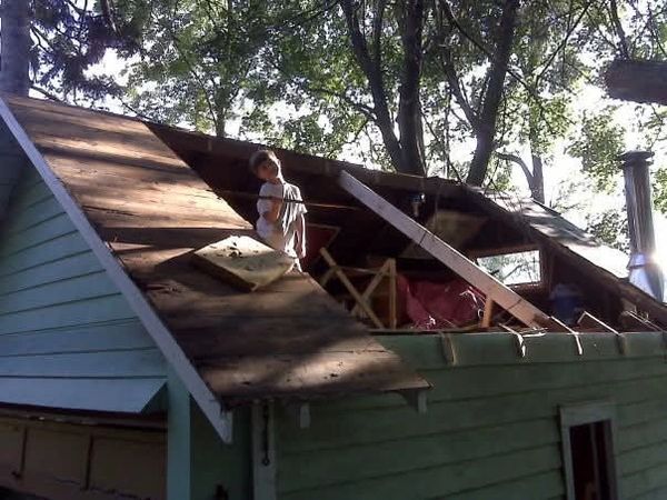 A person working on a partially removed roof on a house surrounded by trees.