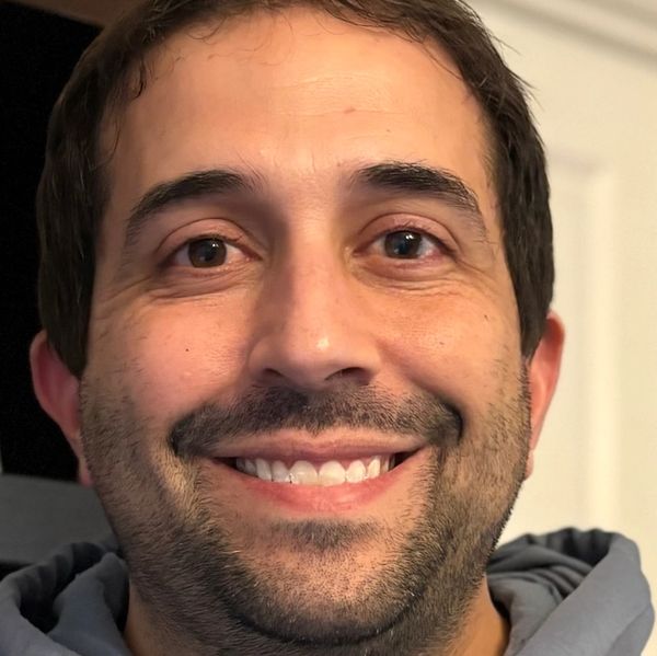 Close-up of a smiling man with dark hair and facial hair.