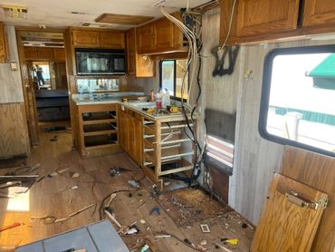 Interior of a rundown RV with damaged cabinets and exposed wiring.