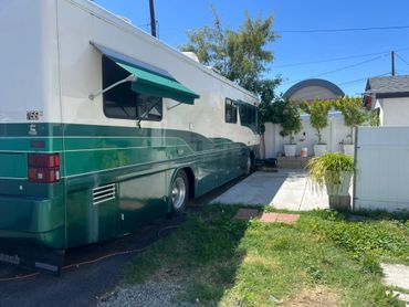 A green and white RV parked beside a house under a clear blue sky.