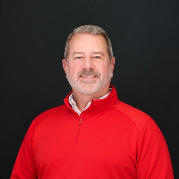 Smiling middle-aged man in a red pullover against a black background.