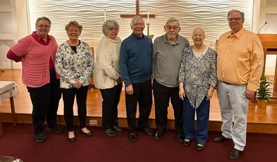 Group of seven elderly people standing inside a church near a cross.