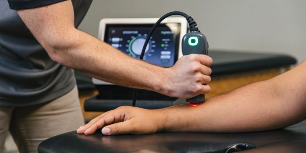 Therapist using laser therapy on patient's wrist.