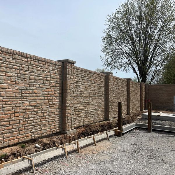 Stone-patterned concrete fence with a gravel ground and construction framework.