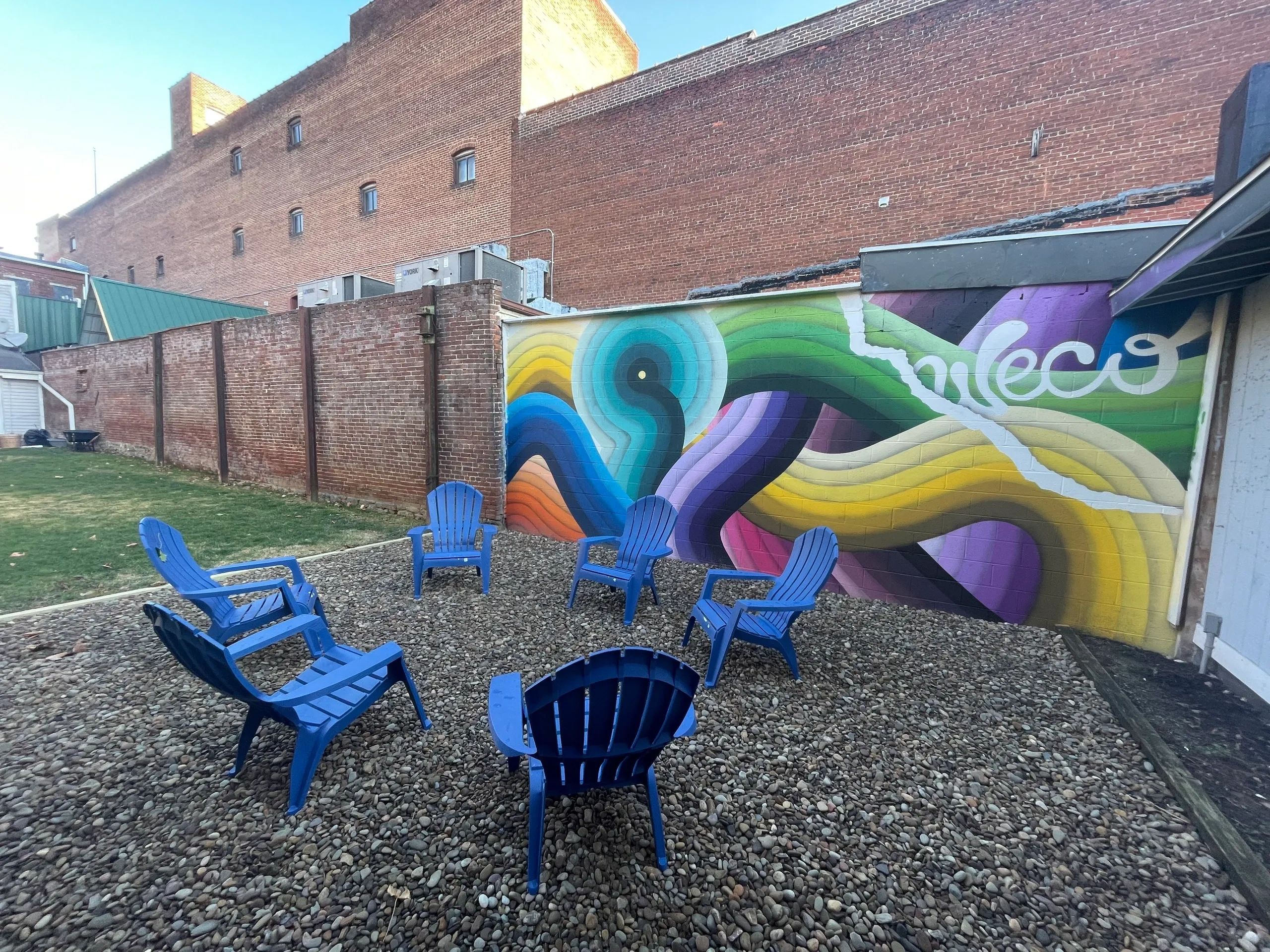 Outdoor seating area with blue chairs and colorful mural on brick wall.