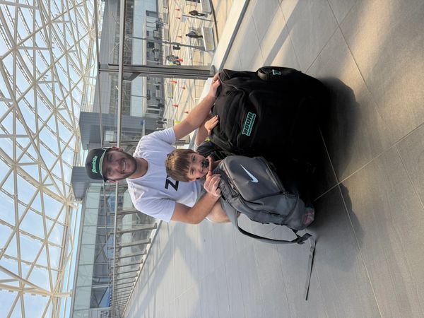 A man and child posing with backpacks at an airport terminal.