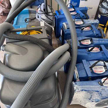Multiple blue air movers and a gray vacuum cleaner with hoses in a storage area.