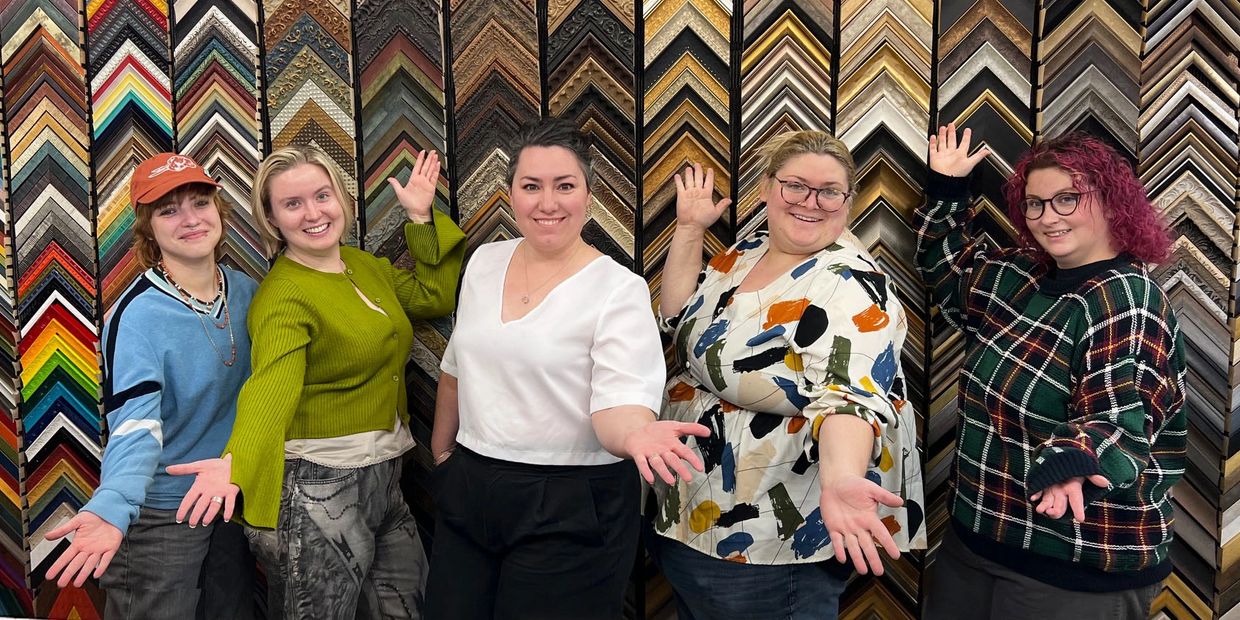 Five women posing happily in front of a wall of colorful picture frames.