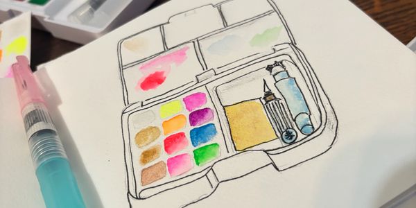 A watercolor paint set being sketched and painted in a notebook.