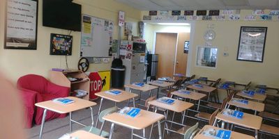 Empty classroom with desks and chairs arranged, each with a book on top.