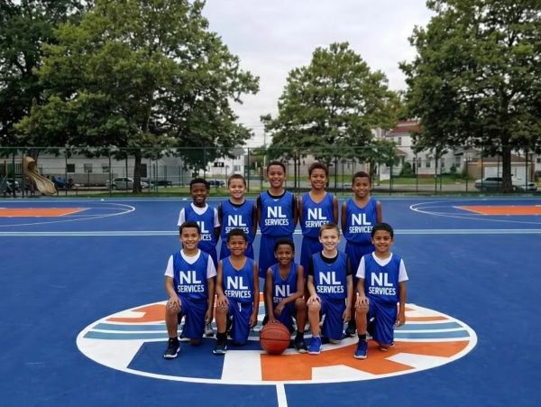 Youth basketball team posing on a blue court with NL Services jerseys.