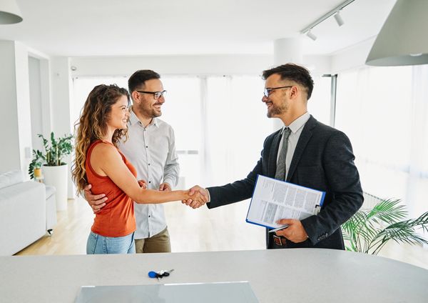 Real estate agent shaking hands with a young couple in a bright room.