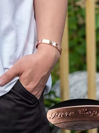 Hand wearing a rose gold bracelet with "Pure Copper" engraved.