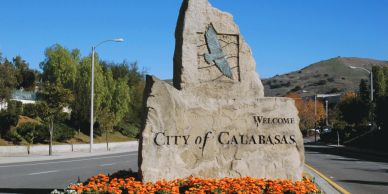 Stone welcome sign for City of Calabasas with flowers and hills.