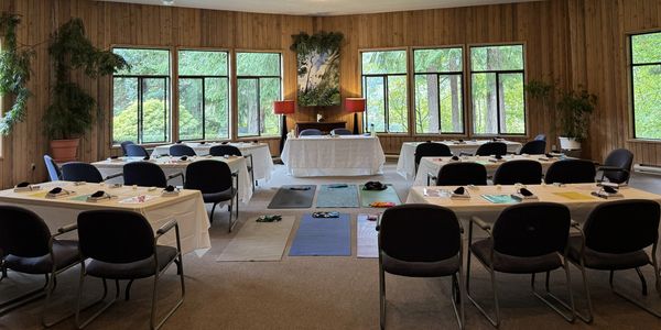 A cozy conference room with tables, chairs, and yoga mats by large windows.