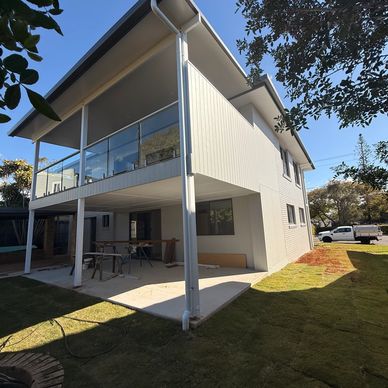 Modern two-story white house with glass balcony and spacious yard.