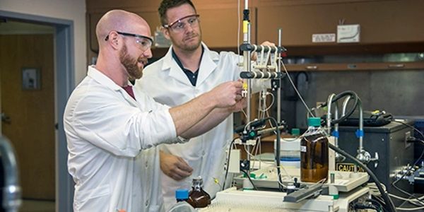 Two scientists in a lab conducting an experiment with glassware and equipment.