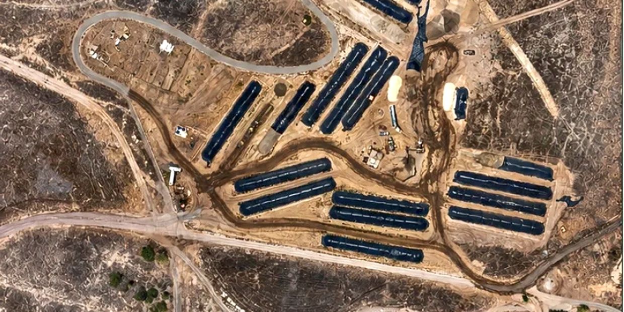 Aerial view of a large construction or industrial site with dark rectangular tanks and dirt roads.