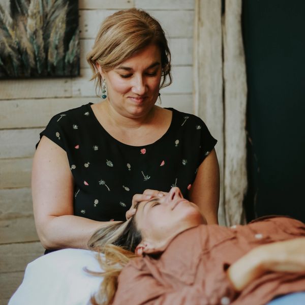 A woman gently massages another woman's head in a cozy setting.