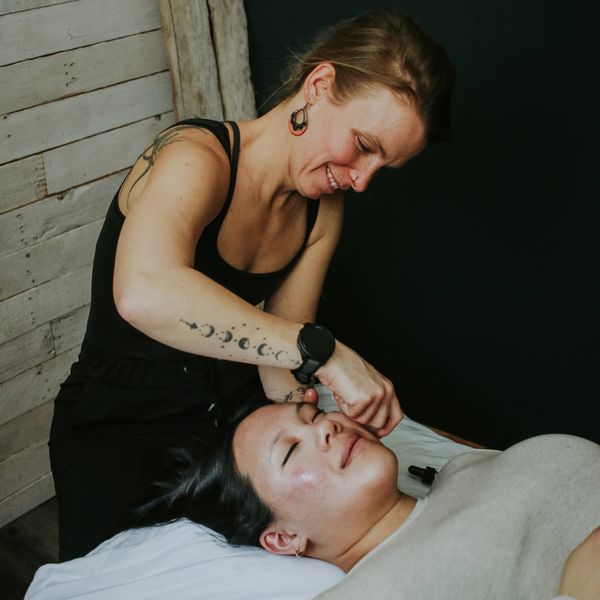 A woman giving a facial treatment to a relaxing client.
