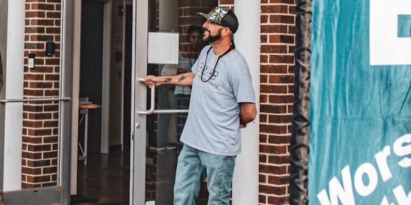 Man holding door open outside a brick building entrance.