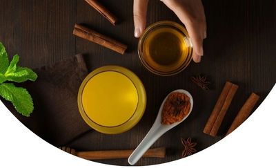 Top view of ingredients including cinnamon sticks, turmeric powder, honey, and mint leaves on a dark wooden surface.