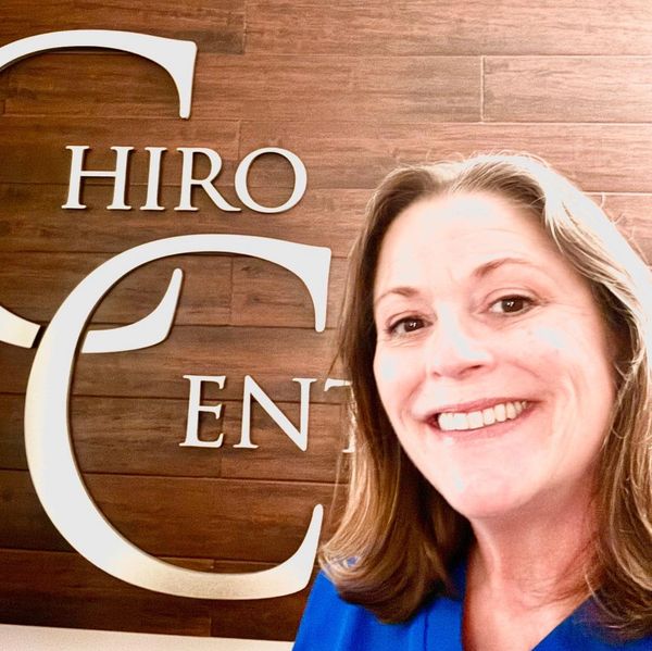 Smiling woman taking a selfie in front of a wooden wall with large white letters.