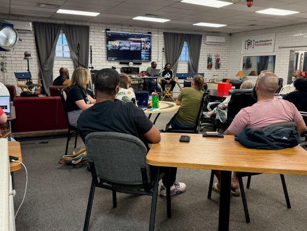 Group meeting in a casual room with a screen and various seating arrangements.
