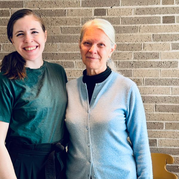 Two women smiling together against a brick wall background.