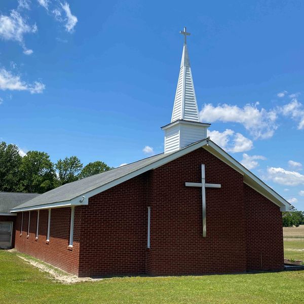 A brick church with a white steeple and cross under a blue sky.