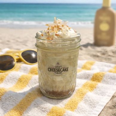 A jar of cheesecake dessert on a beach towel with ocean in background.