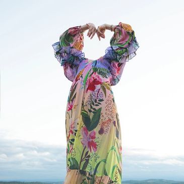 Person stretching in colorful floral dress against sky.