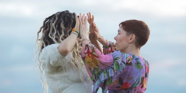 Two women facing each other with raised hands outdoors.