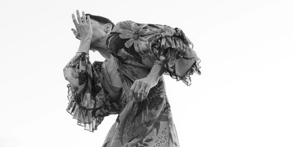Black and white photo of a person in a floral dress covering their face.