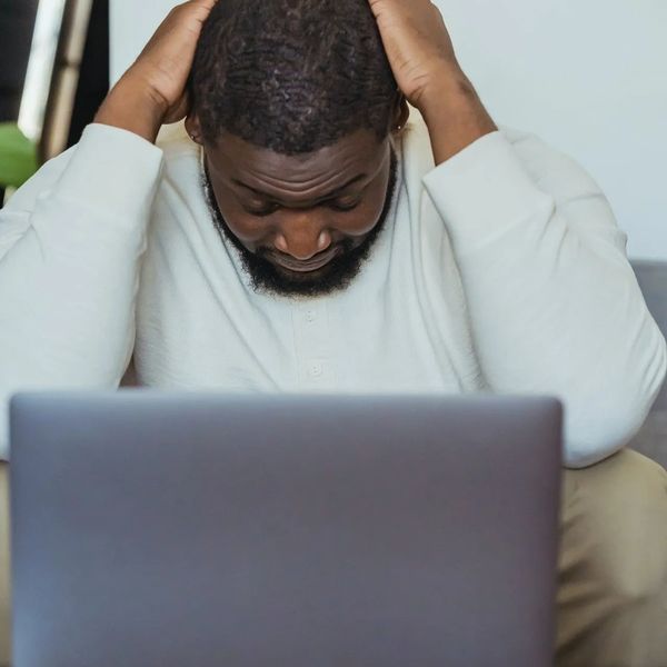 Image of man holding head in hands in despairing gesture with laptop open in front of him - Photo co