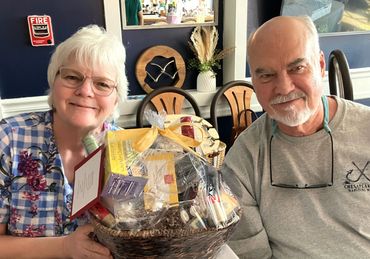 Smiling elderly couple holding a gift basket indoors.