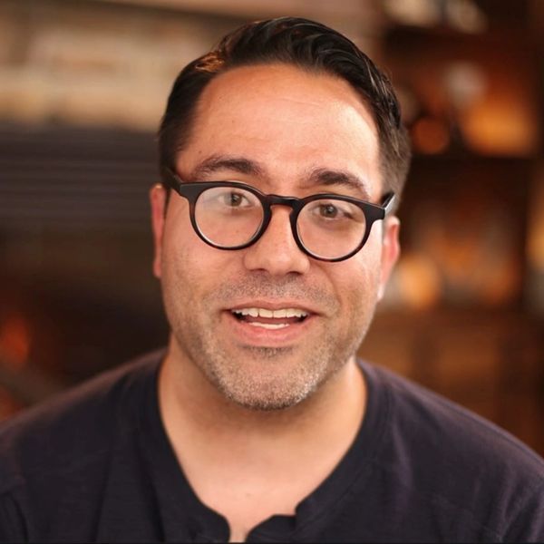 Man with glasses smiling in a warmly lit room.