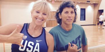 Two women smiling and making shaka signs inside a gymnasium.