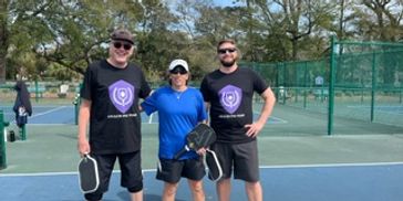 Three people posing with pickleball paddles on an outdoor court.