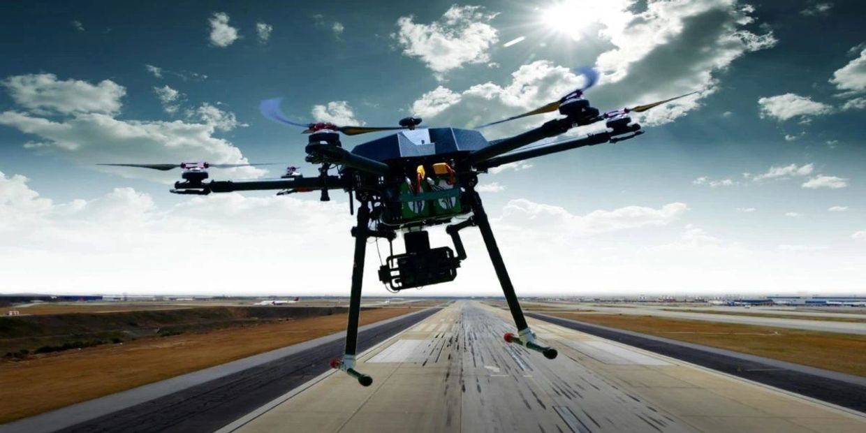 A drone flying over an airport runway under a bright sky.