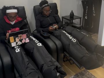 Two people relaxing in massage chairs with compression leg boots.