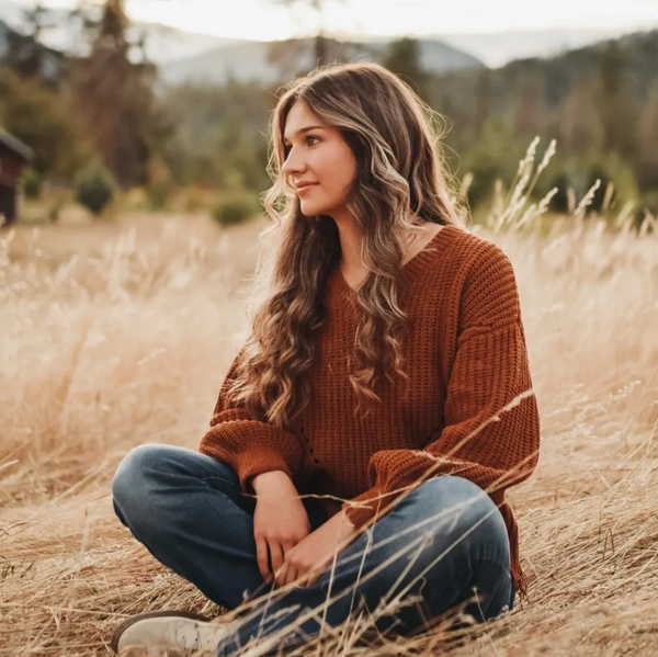 Young woman in a cozy sweater sitting in a field of tall dry grass.