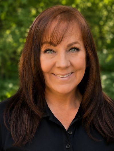 Smiling woman with long brown hair outdoors, wearing a black shirt.