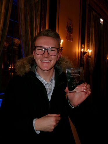 Young man smiling and holding an award in an elegant room.